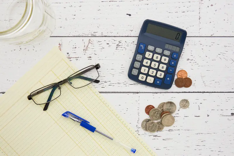 Calculadora, moedas, óculos e caneta sobre papel amarelo