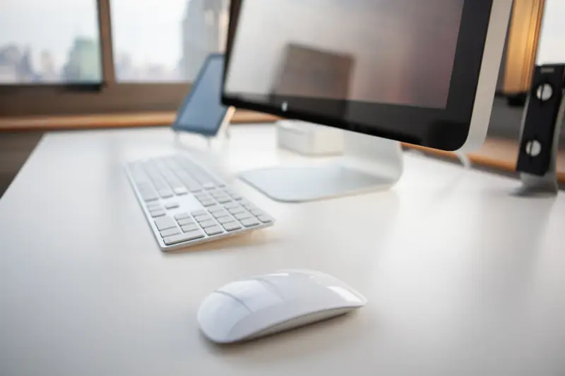 Computador de mesa com teclado e mouse numa mesa branca, onde o MEI faz o cadastro e emite a nota