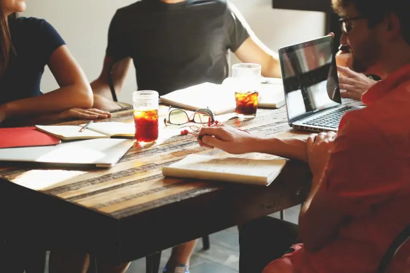 Pessoas reunidas em volta de uma mesa com notebook e anotações