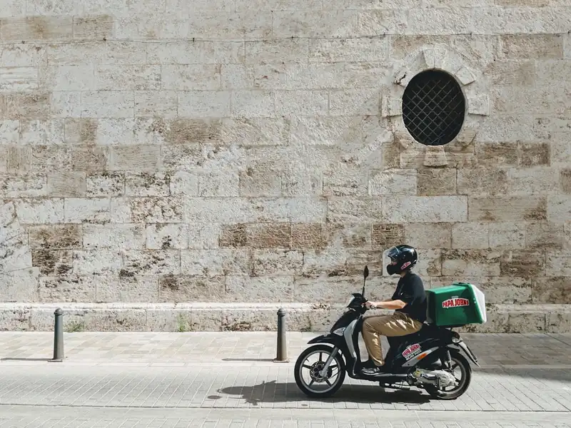 Entregador de moto com a mochila térmica de entregas nas costas, parado em uma rua da cidade