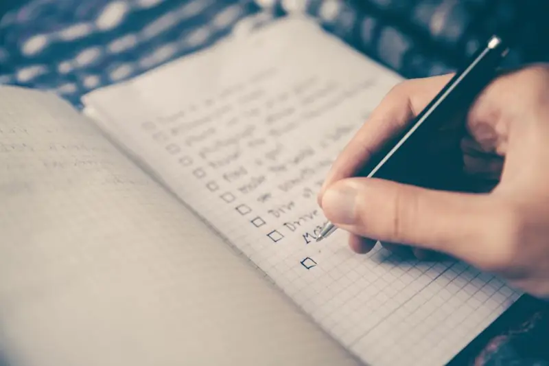 Mão marcando uma lista de tarefas num caderno, como a lista de serviços de uma nota fiscal