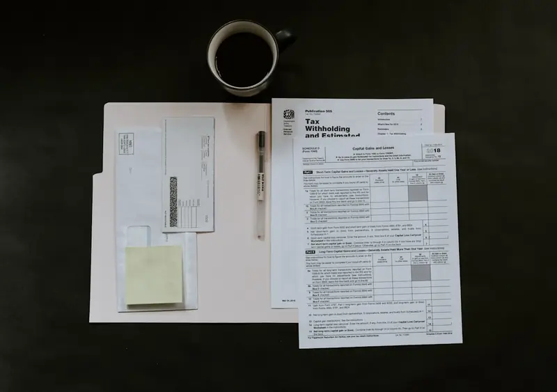 Notas fiscais impressas e um notebook aberto sobre a mesa de trabalho, com uma caneta ao lado