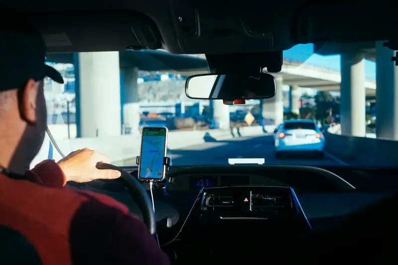 Motorista de aplicativo ao volante com o celular no suporte mostrando o aplicativo de corridas aberto