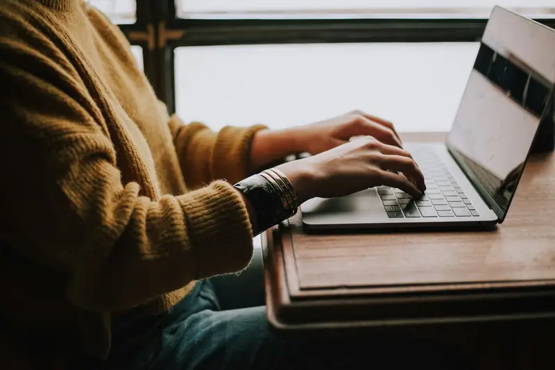 Pessoa preenchendo um formulário no notebook sobre a mesa, com as mãos no teclado e a tela mostrando campos de cadastro