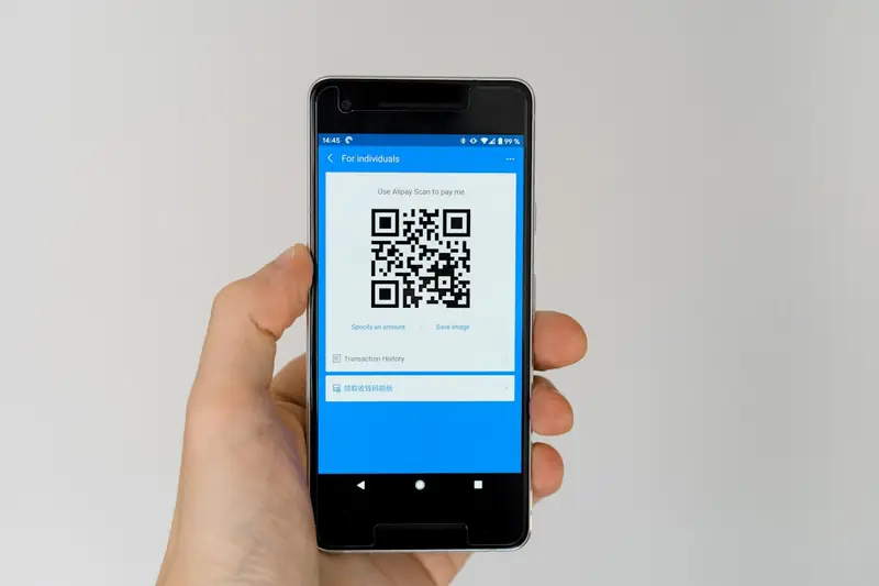 Cliente pagando por Pix com o celular, lendo um QR code no balcão de um pequeno comércio