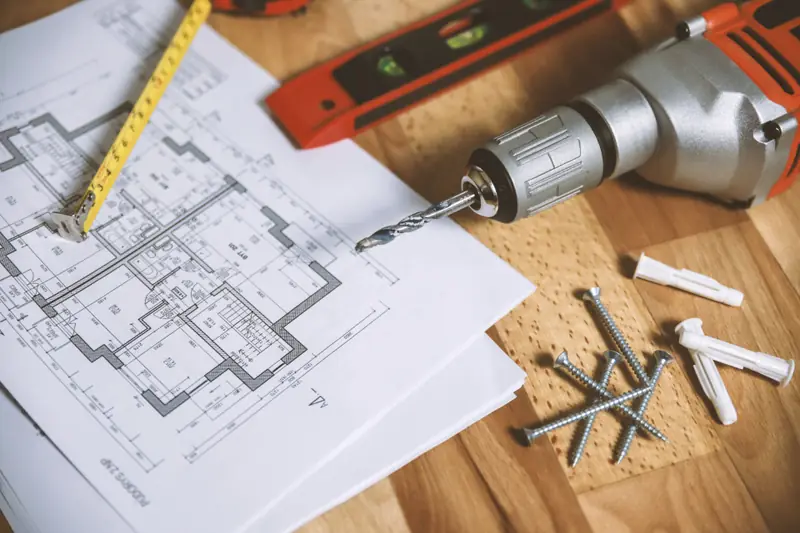 Planta de obra sobre a mesa com furadeira, trena e buchas