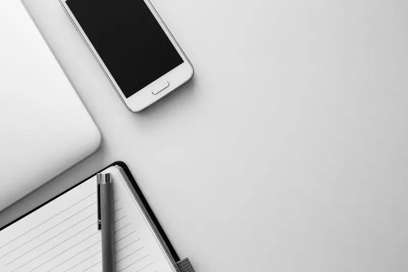 Celular sobre uma mesa branca ao lado de um caderno